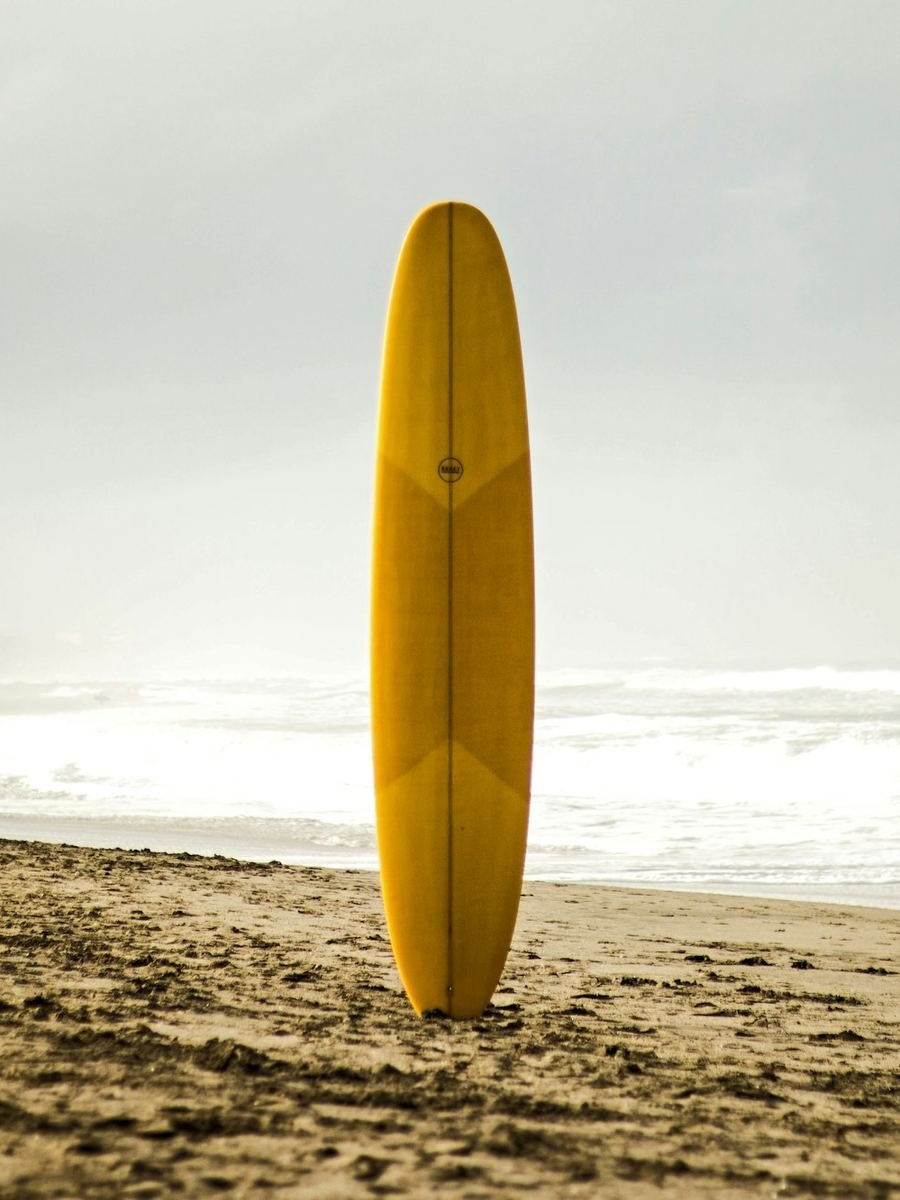 Prancha de surf fincada na areia, com o mar ao fundo